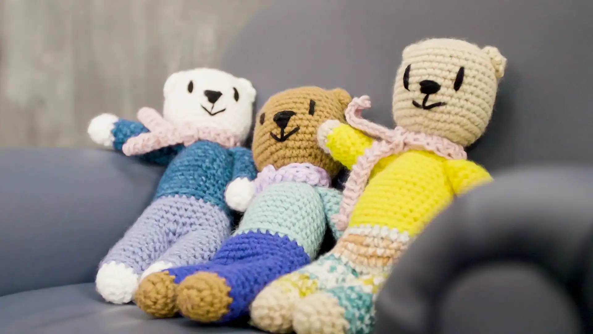 A trio of JereBear crocheted teddy bear sit on a couch