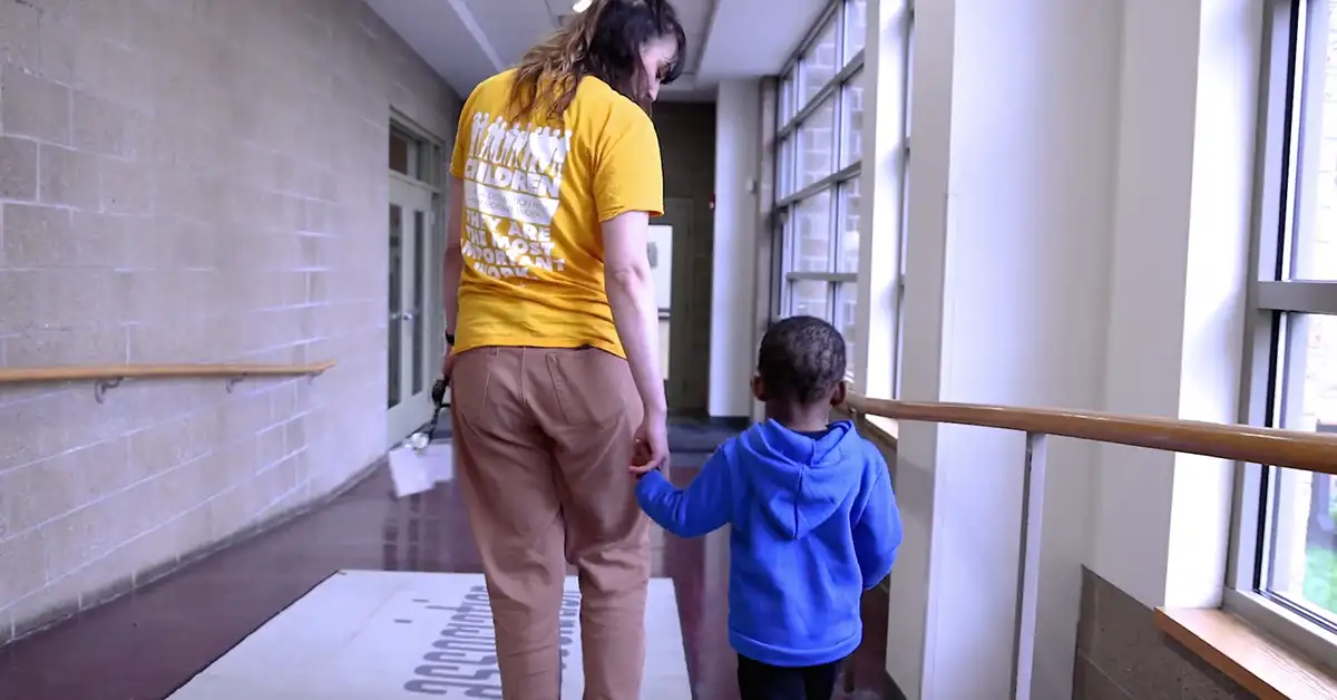 A child and caregiver walking through the halls of the Kindsley Center Association at Jeremiah's Place